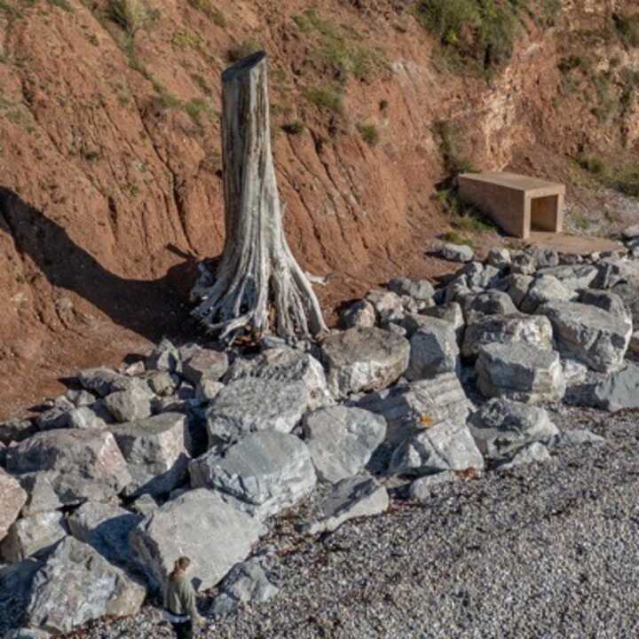 Rocky shore with large boulders and a wooden structure against a clay cliff.