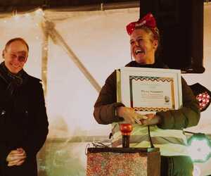 Two people at an event, one holding a certificate, festive setting with lights.